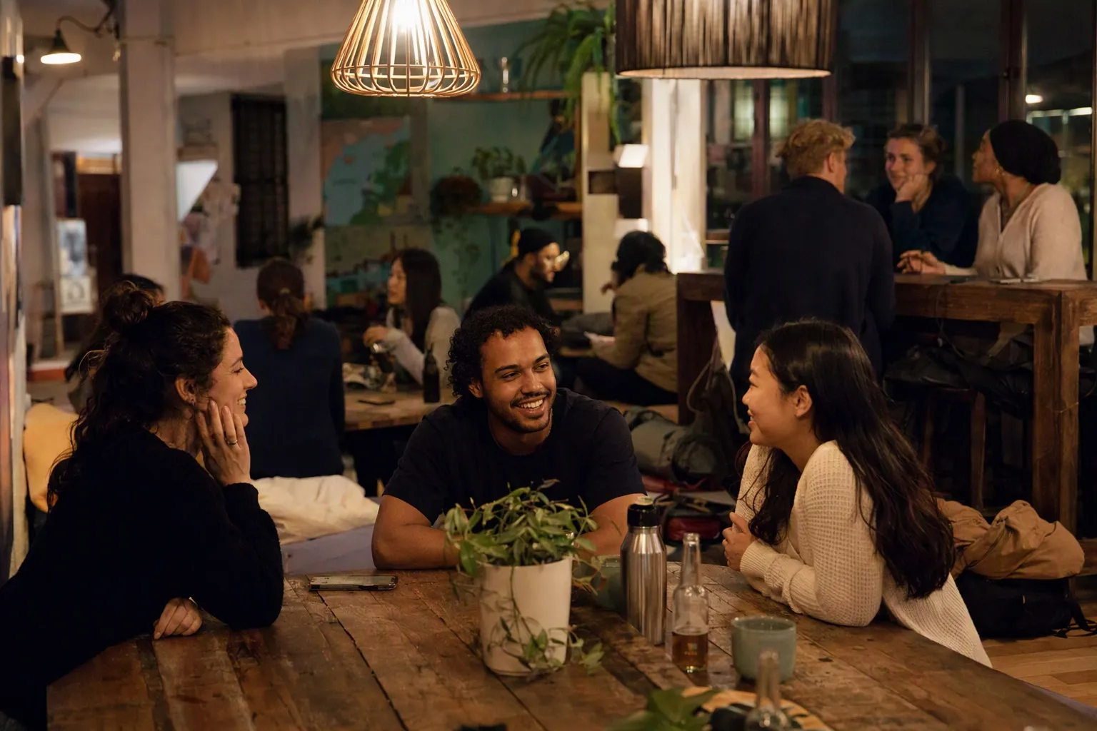 People talking around a communal table in a hostel common room in the evening