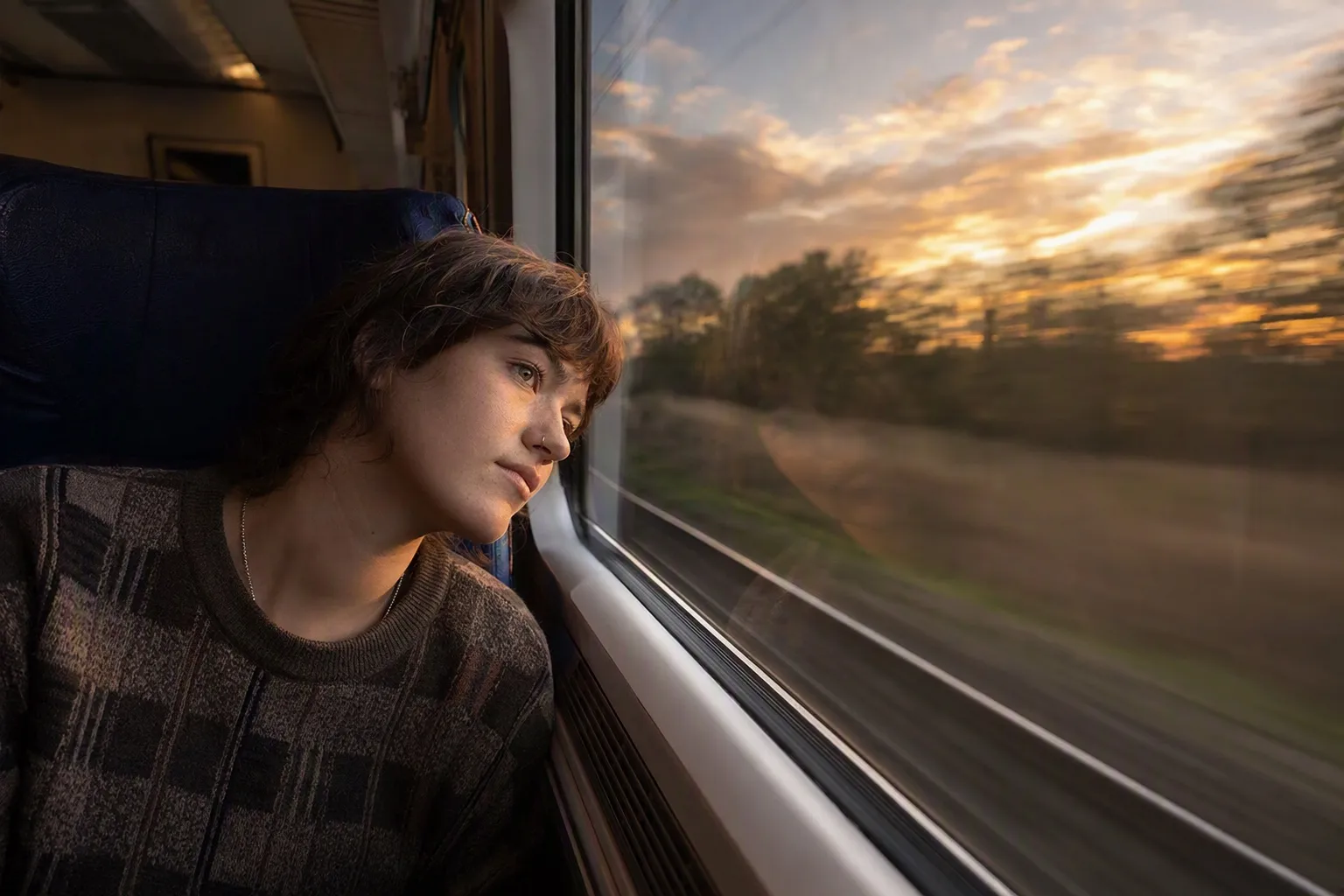 A solo traveller looking out of a train window at sunset